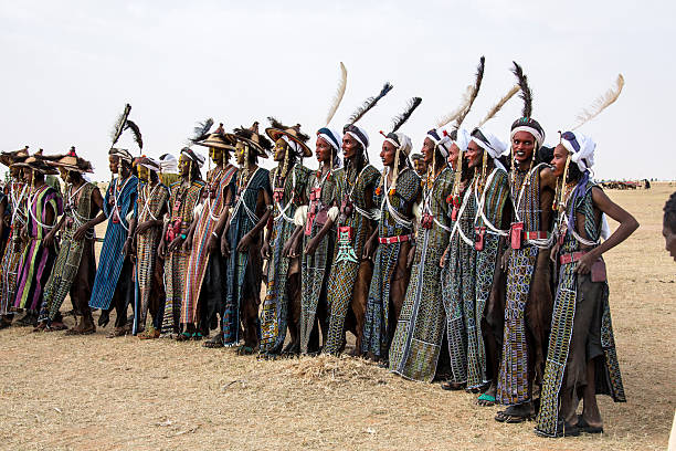 Longue file de danseurs Wodaabé en tuniques brodées et coiffes à plumes lors du Guéréwol